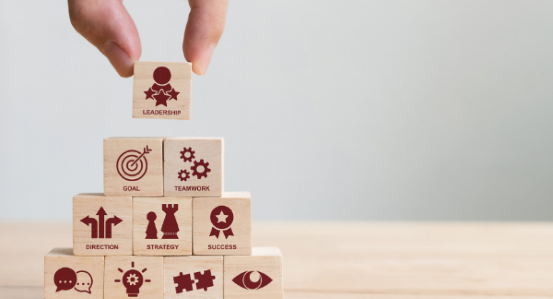 Wooden blocks stacked in a pyramid: Communication, Solution, Partnership, Vision, Direction, Strategy, Success, Goal, Teamwork, Leadership